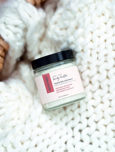 Jar of toasted coconut body butter on a textured white surface